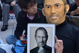 Một khách hàng đeo mặt nạ Steve Jobs và cầm chiếc iPad có khuôn mặt của Steve Jobs, ngồi trước cửa hàng Apple Store ở Tokyo trong ngày 20/9/2013.