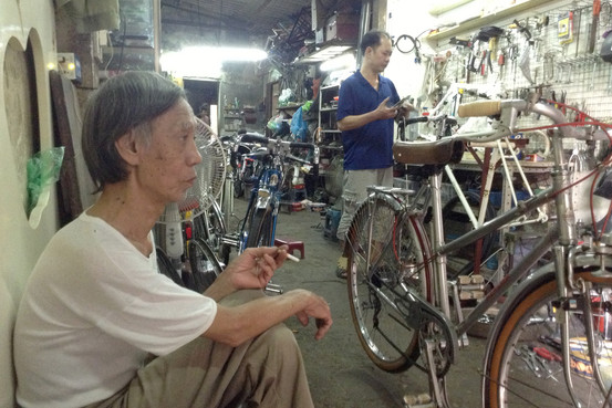 Ông Trần Anh Vũ (bên trái) đang ngồi trong tiệm sửa xe trong một ngõ nhỏ cạnh Hồ Tây, nơi được coi là bảo tàng xe đạp cổ thu nhỏ.