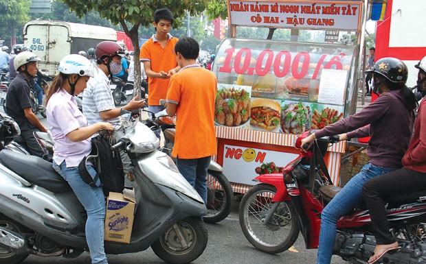 bánh mì Thổ Nhĩ Kỳ đến bánh mì Hậu Giang, bánh mì Xì Gòn… nhưng chỉ 10.000 đồng/ổ. 6h30 sáng, tại xe bánh mì Cô Hai Hậu Giang gần góc đường Cộng Hoà và Út Tịch, dòng xe nối đuôi kéo dài từ trong hẻm tràn ra đường, ai cũng trong tư thế vội vã để chờ mua những ổ bánh mì nóng, giòn chỉ với giá 10.000 đồng/ổ. Ai thích nhiều nhân thì có thể mua giá 15.000 đồng/ổ. Khách đa số là nhân viên đi làm, học sinh đi học… Vỉa hè sôi động “Bánh mì của em có 20 loại nhân như xíu mại, nem nướng, chả cá, xúc xích, trứng, chà bông, chả lụa… Đặc biệt, có món thịt khìa nước dừa bán mau hết nhất. Món này, người miền Tây chuộng và thường chế biến trong bữa cơm gia đình”, Tuyết Xuân, cô chủ của xe bánh mì cô Hai Hậu Giang hoạt bát kể trong khi hai tay vẫn đang thoăn thoắt trở từng ổ bánh mì trên bếp than hồng. Vì cô chủ là người gốc miền Tây nên muốn đem hương vị quê nhà chia sẻ với người thành phố. “Công thức ướp thịt em học từ bà và mẹ em, còn chả cá là do mẹ làm và gửi từ quê lên”, Xuân thổ lộ.  Xếp hàng mua bánh mì cô Hai Hậu Giang.