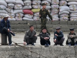 Người dân CHDCND Triều Tiên ngồi ở bờ sông Yalu thuộc thành phố Sinuiju đối diện thành phố Đan Đông Trung Quốc . Phía sau họ là những bao hàng nông sản - Ảnh: Reuters